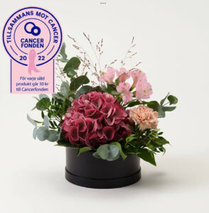 Rund hattask med blomsterdekoration i lila/rosa. Beställ hos Interflora!