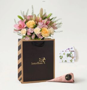 Presentpåse med floristbunden bukett i milda pastellfärger, en chokladstrut och ett lyxigt morsdagskort. Beställ som blomsterbud hos Interflora!